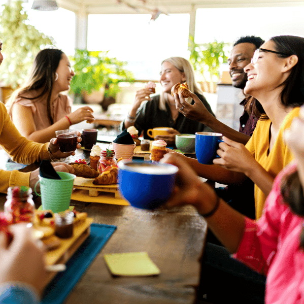 Vrienden aan een houten tafel met koffie, croissants, cupcakes en potjes jam