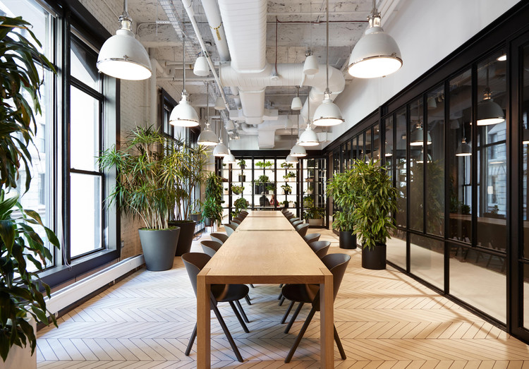 Lange houten tafel met stoelen in een licht kantoor met planten en hanglampen