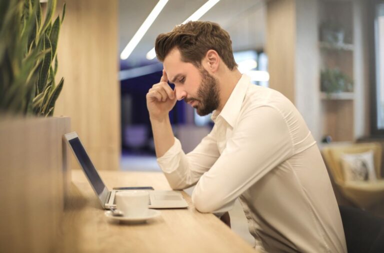 Een man met zijn hand tegen zijn voorhoofd kijkt bedenkelijk naar zijn laptop