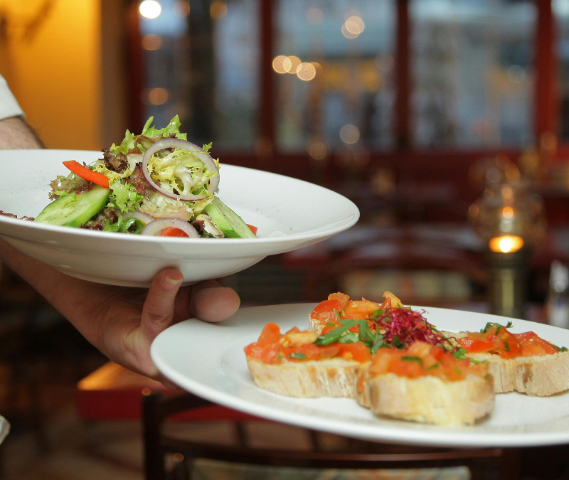 Ober draagt een salade en bruschetta door een restaurant